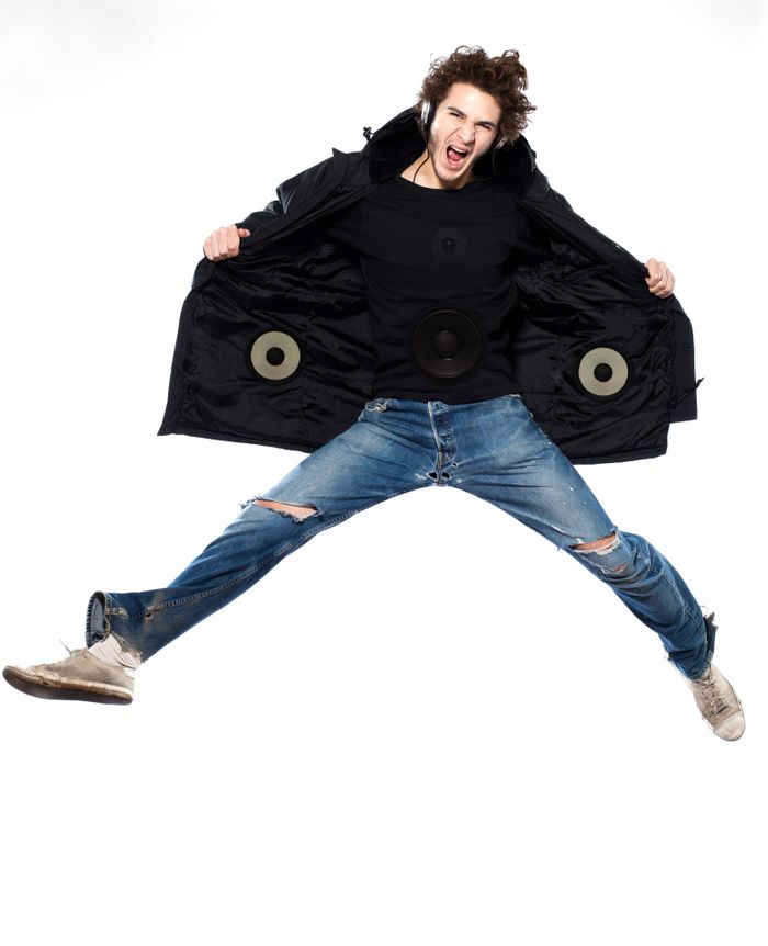 A young man jumping up into the air and holding open his black jacket. Inside the jacket are a pair of speakers.